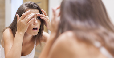 Shocked woman squeezing pimple in bathroom